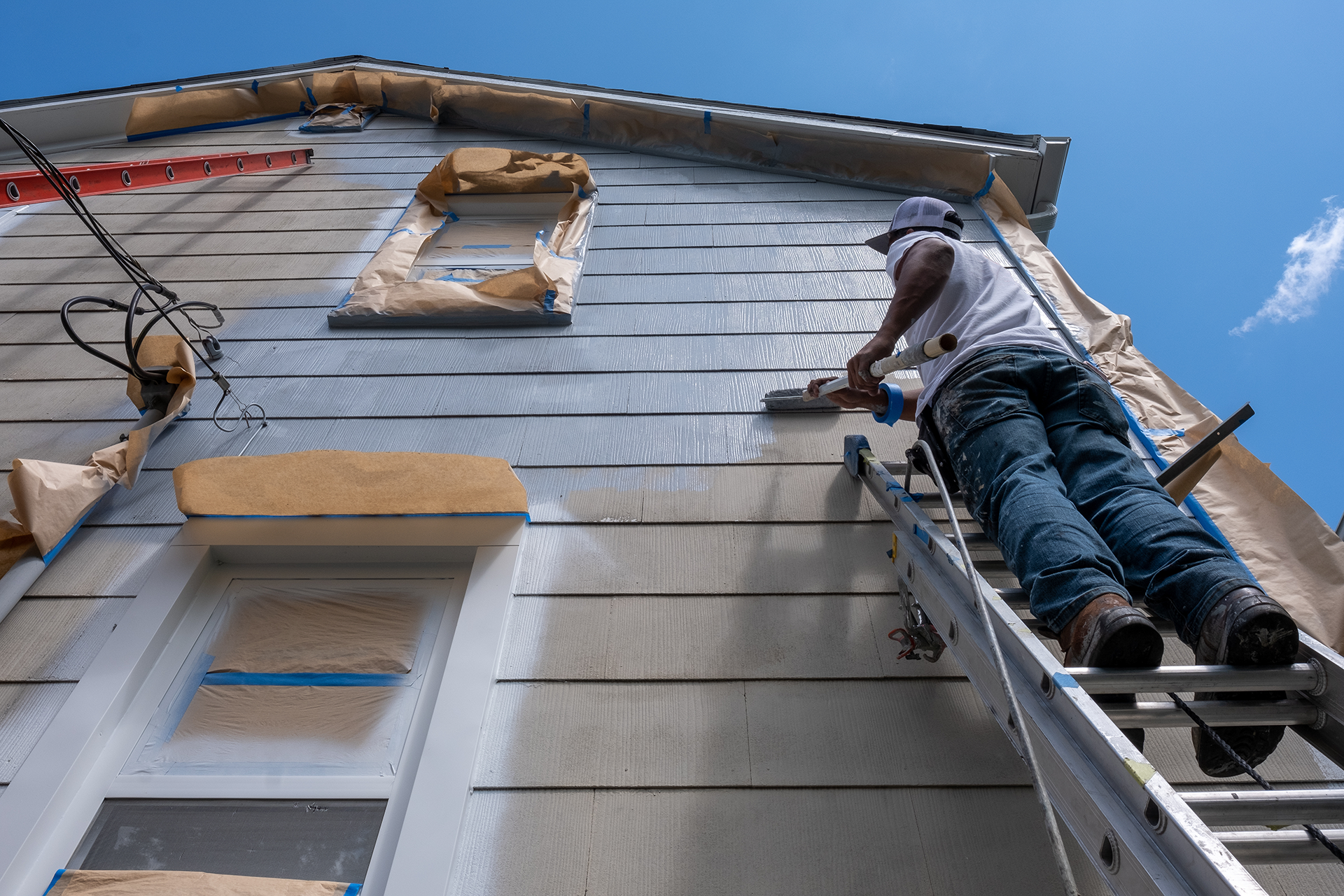 Worker applying fresh paint with roller at top of siding wall